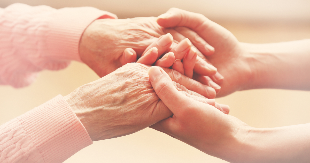 Close-up of a caregiver gently holding the hands of an elderly person, symbolizing compassion, trust, and in-home care support.