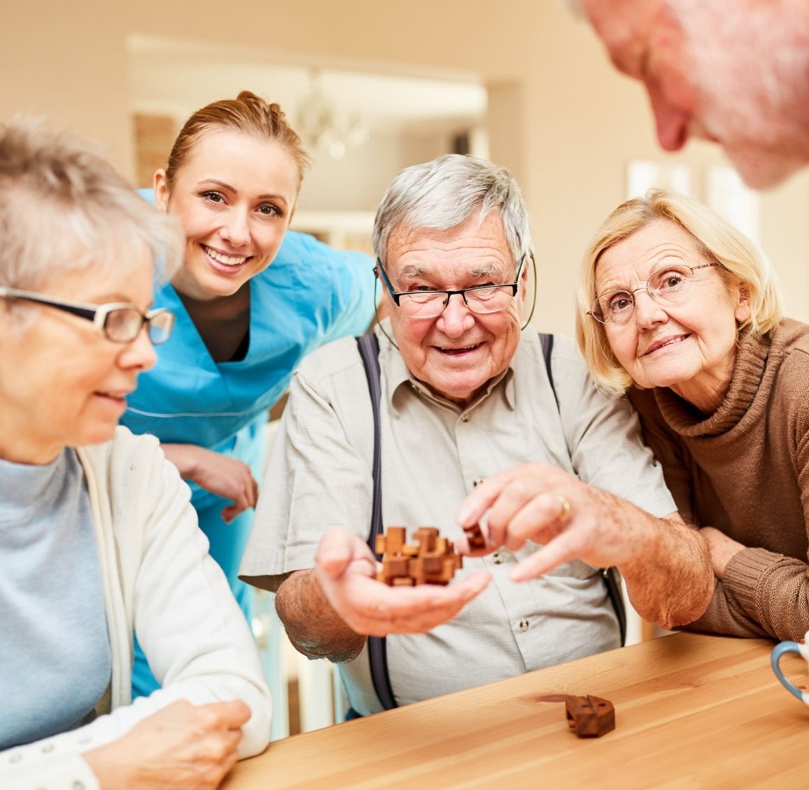 A caregiver and a group of older adults gather around a table, smiling and working together on a wooden puzzle, representing mental stimulation, social interaction, and supportive senior care.